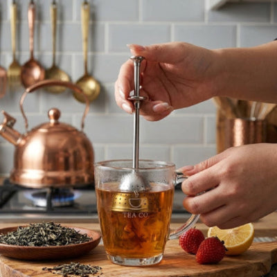 main tenant infuseur a the dans un verre de the